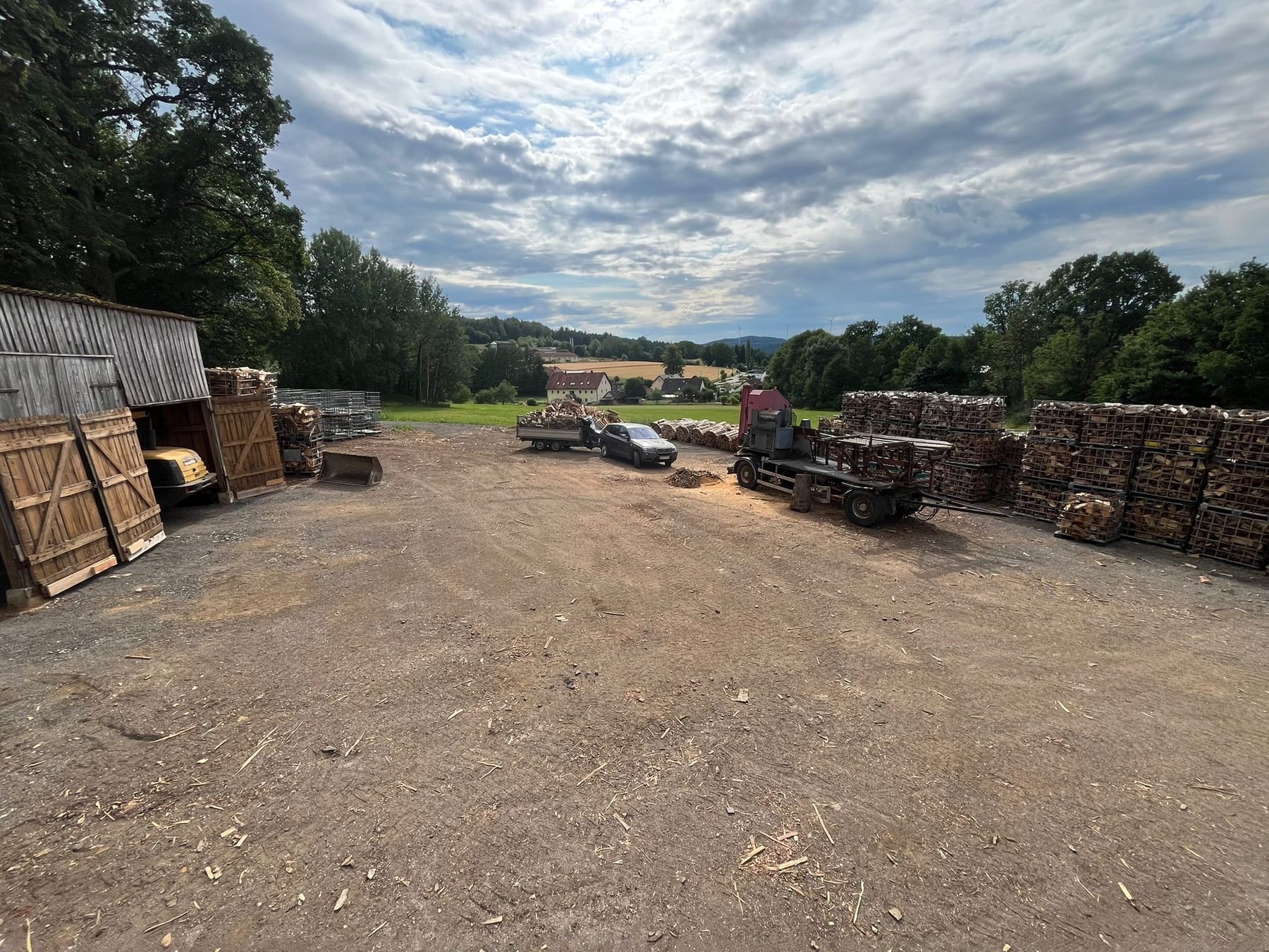 Weiter Blick über den Holzplatz mit Schuppen, Spalter und Gitterboxen