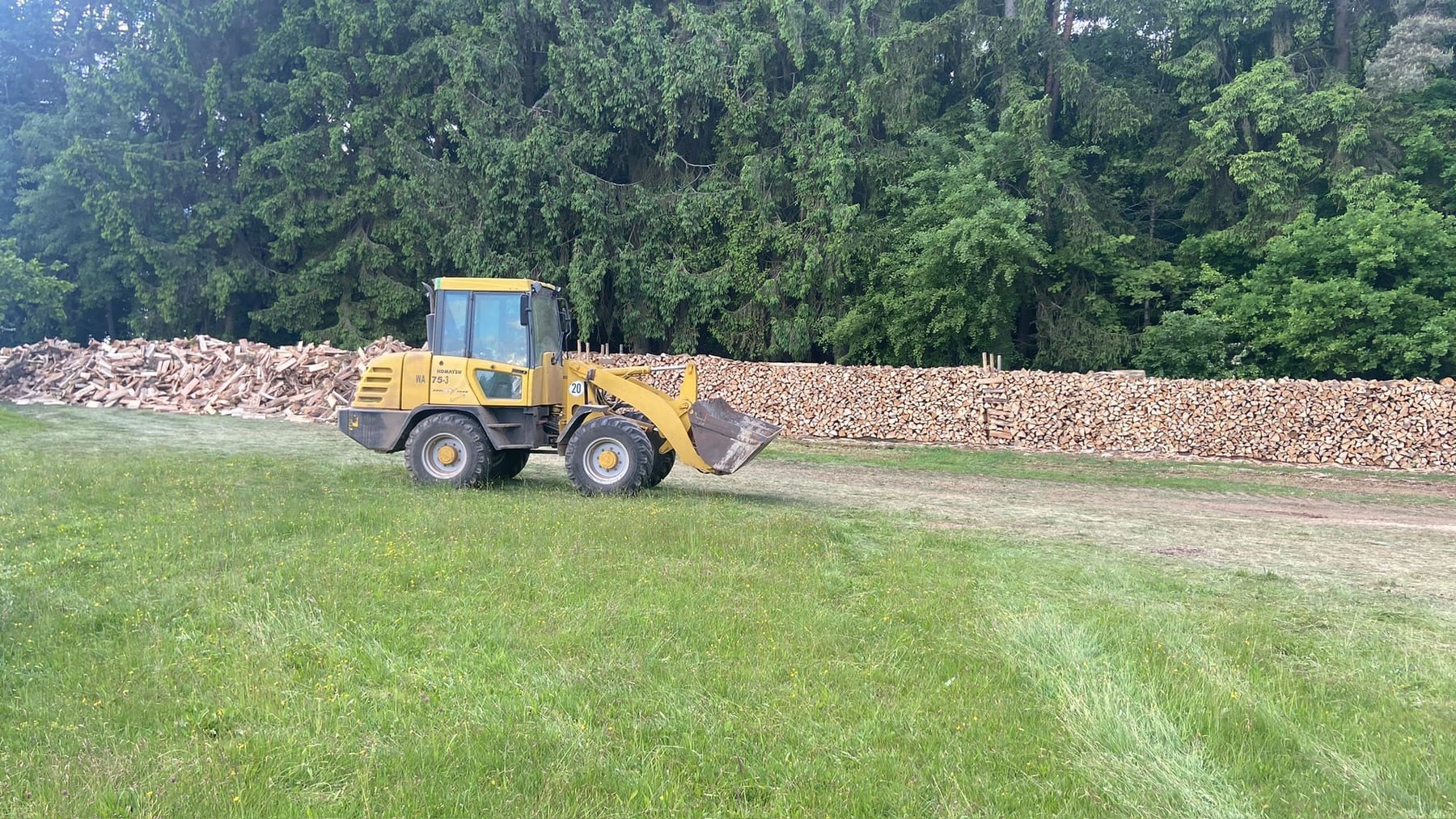 Eine lange Wand aufgesetzter Scheite am Waldrand, davor der Radlader: So lagert das Holz an der Luft